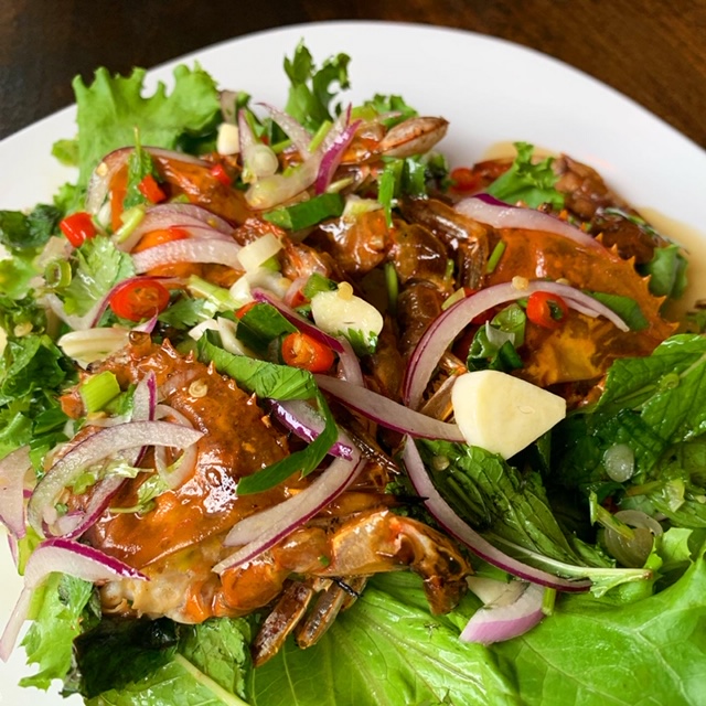 A plate of grilled soft-shell crab on a bed of lettuce with red onions, tomato, and drizzled in sauce.