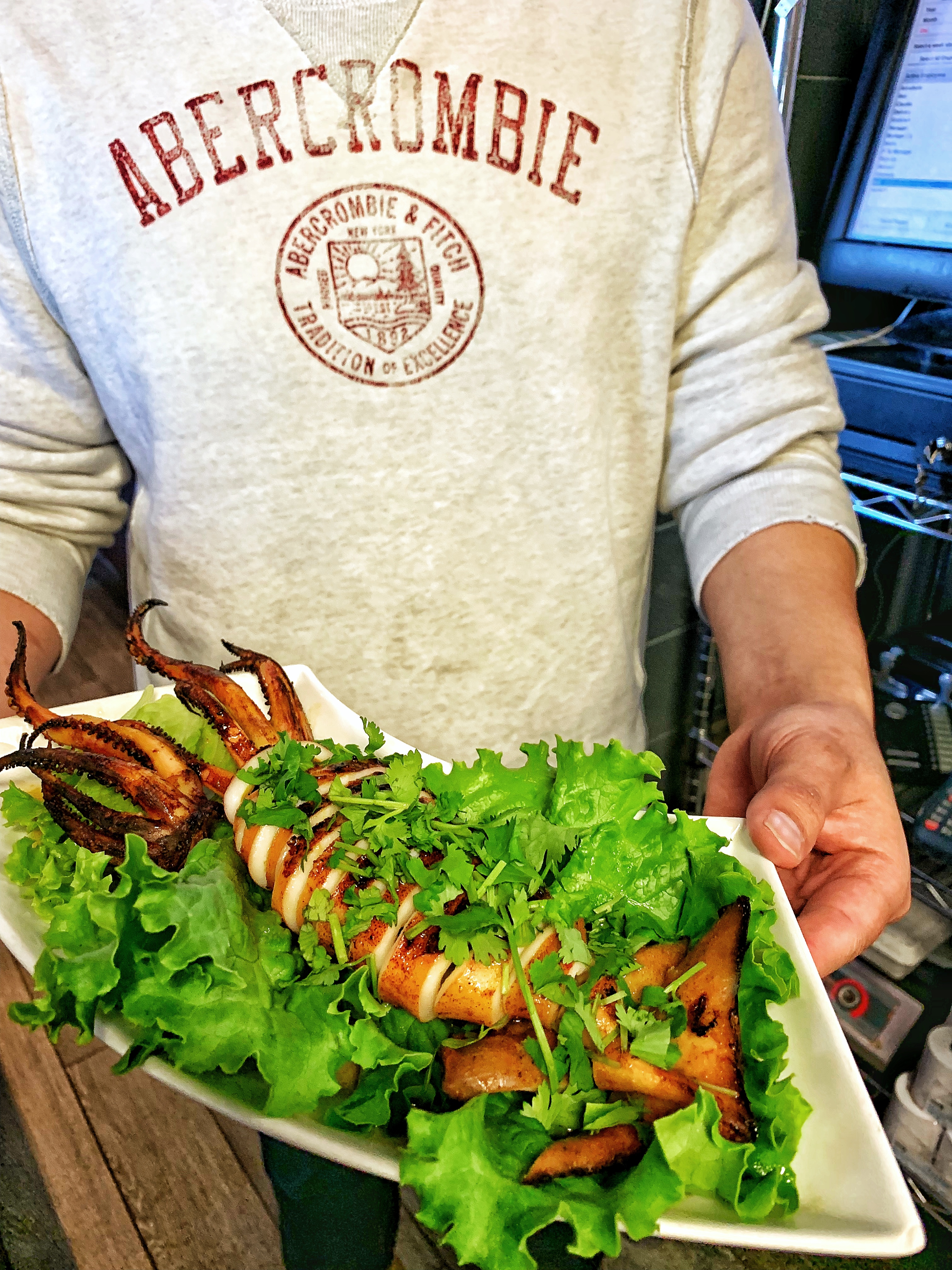 A server holding a plate of Grilled Squid on a bed of lettuce.