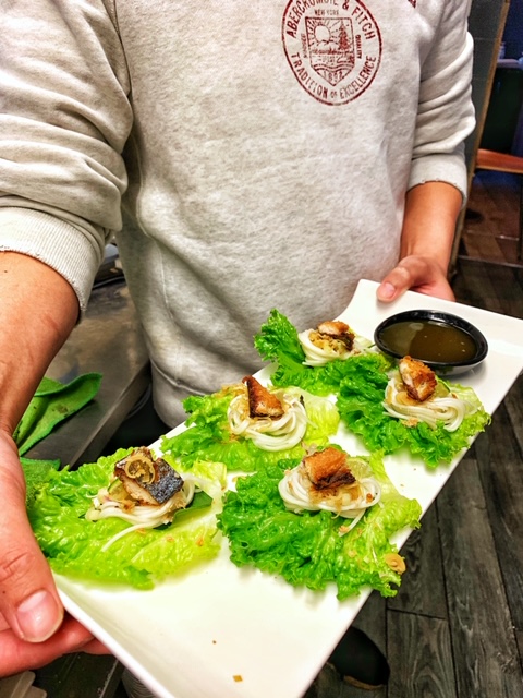 A server holding a plate of Mieng Pla Too on a bed of lettuce and with dipping sauce.