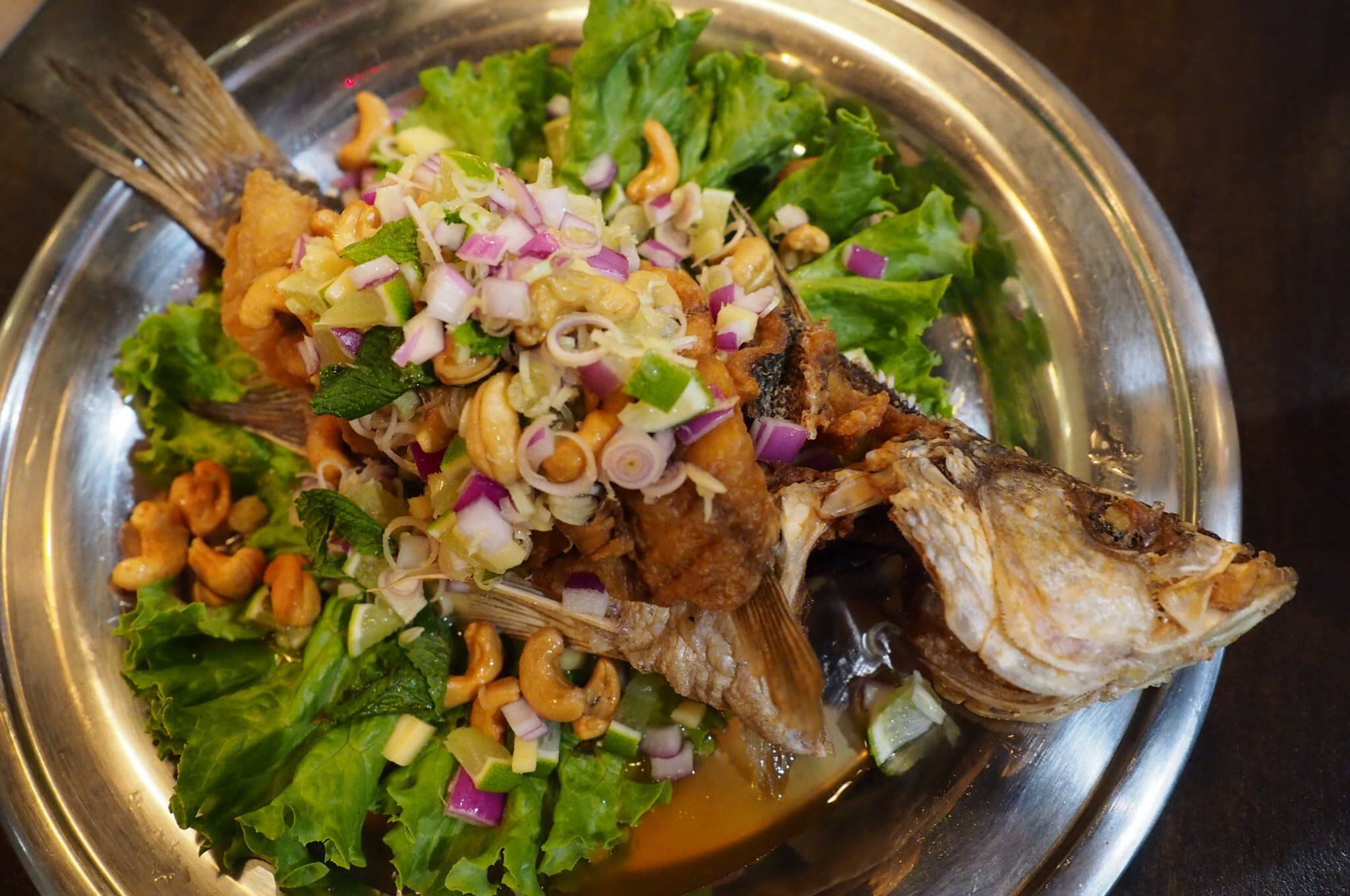 Grilled fish served with lettuce, cashews, red onions, and cilantro.