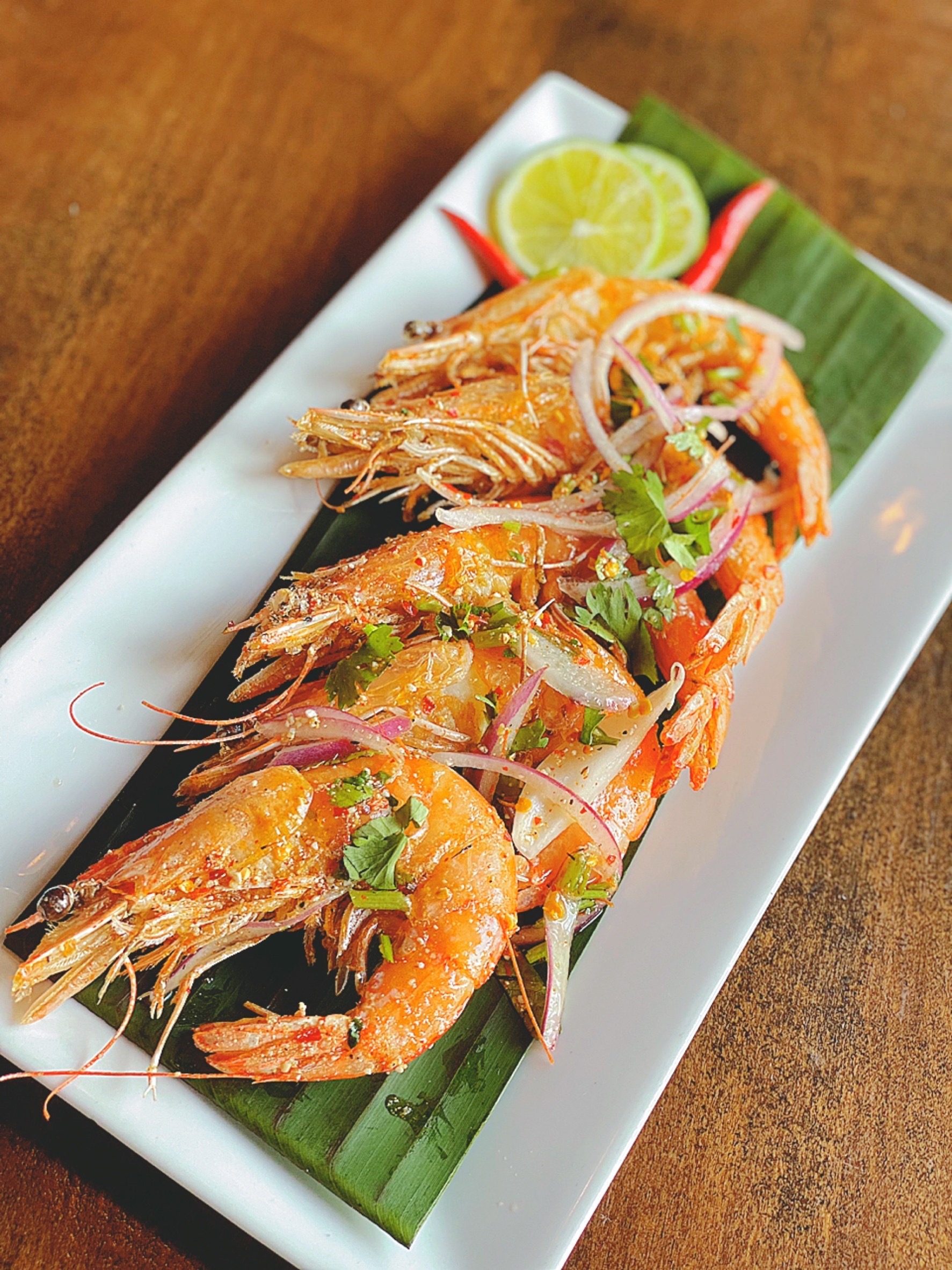 Large prawns resting on a bamboo leaf and white plate.